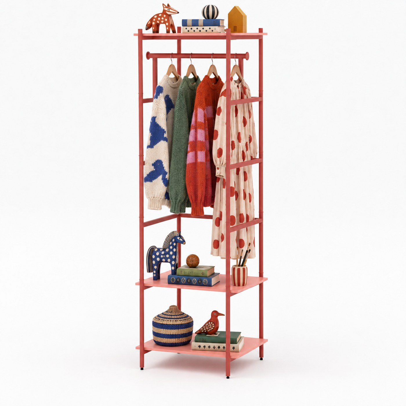 A slim coral frame with three jumpers and a dress on the rail, and books, a woven basket and painted wooden animals on the two shelves below.
