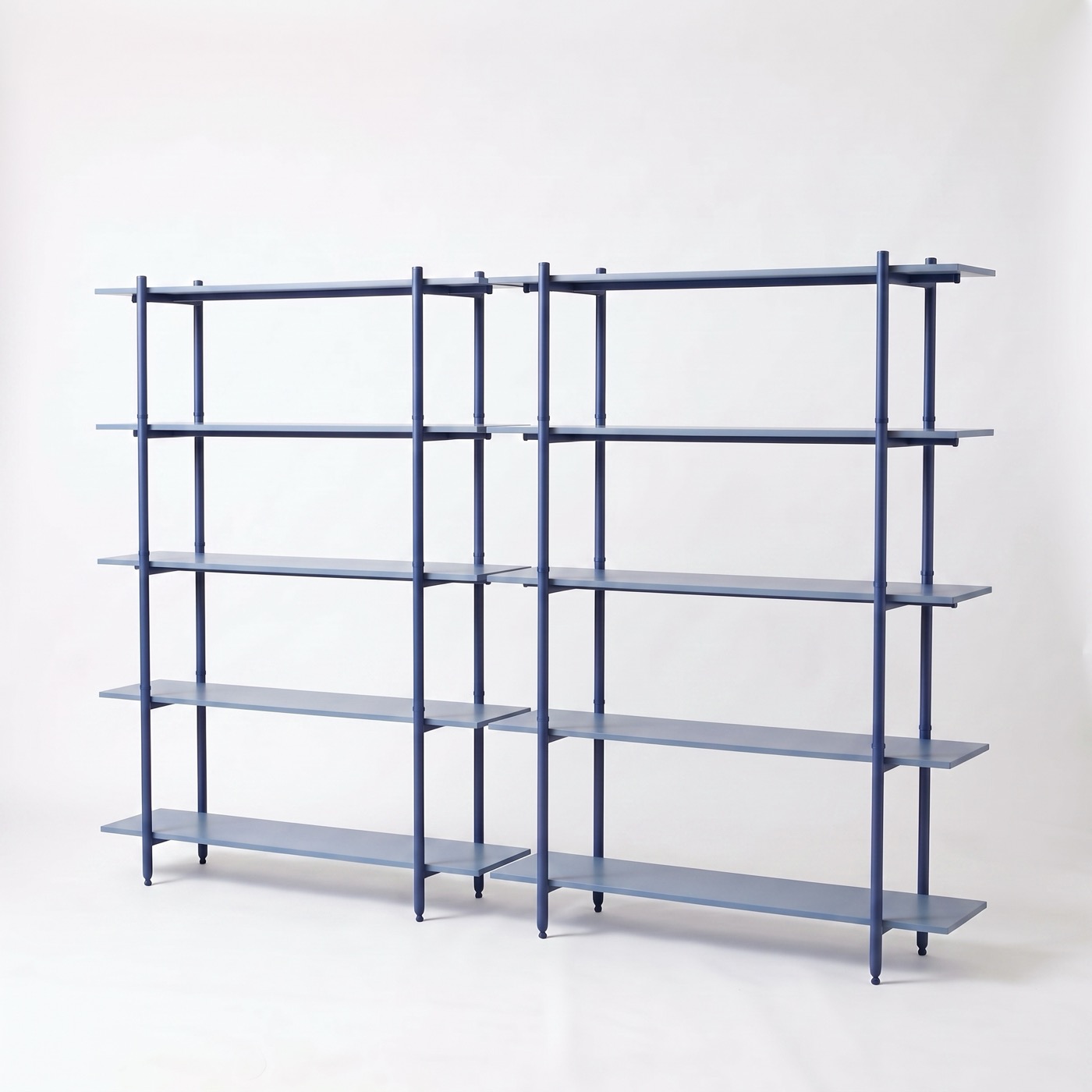 An empty two-bay shelf in marine blue steel, seen from an angle, with five shelves in each bay and no back panel, so the white wall shows through every gap.