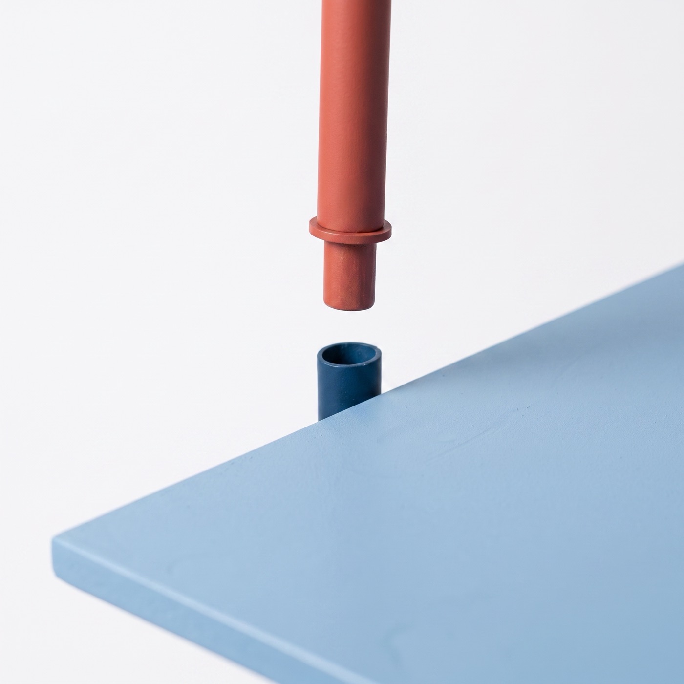 A coral steel post held just above a marine tube on a sky blue board, about to drop into it.