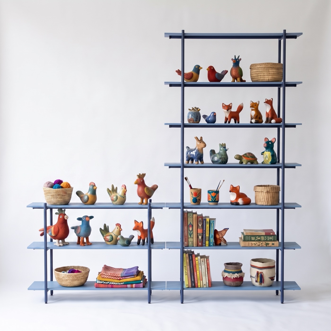 A marine blue steel shelf in two parts, a low three-tier unit beside a tall seven-tier tower, holding painted wooden birds, foxes and other animals, baskets of wool, pots of brushes, books and folded cloth.